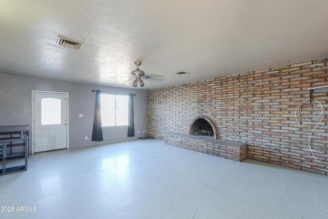 unfurnished living room featuring ceiling fan, a textured ceiling, brick wall, and a fireplace