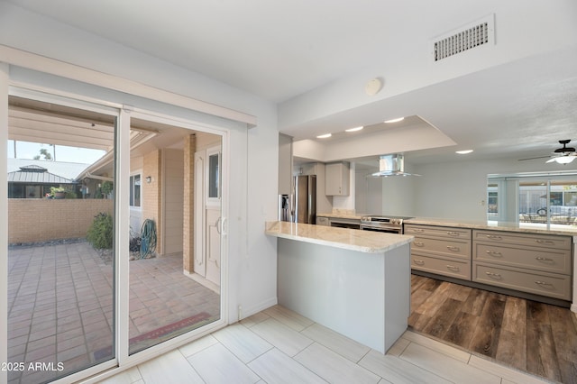 kitchen featuring stainless steel appliances, visible vents, gray cabinetry, wall chimney range hood, and a peninsula