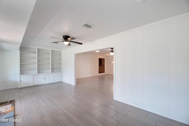 empty room featuring a ceiling fan, visible vents, and built in shelves