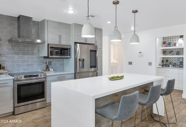 kitchen with stainless steel appliances, a center island, wall chimney exhaust hood, and light wood-type flooring