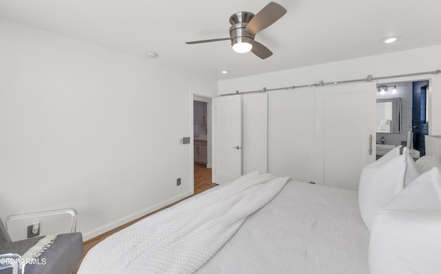 bedroom featuring ceiling fan, a barn door, and wood-type flooring