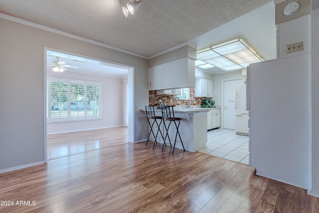 kitchen with a breakfast bar area, white cabinets, white fridge, kitchen peninsula, and light hardwood / wood-style flooring