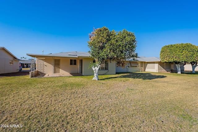 rear view of property featuring a patio, a lawn, and solar panels
