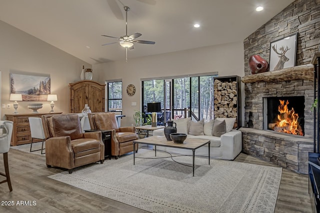 living room featuring high vaulted ceiling, wood finished floors, and a stone fireplace