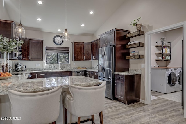 kitchen featuring appliances with stainless steel finishes, washing machine and dryer, dark brown cabinetry, and light wood-style flooring