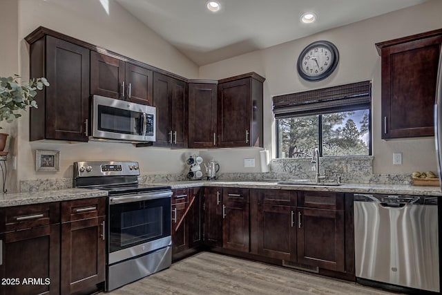 kitchen with light wood-style flooring, light stone countertops, stainless steel appliances, dark brown cabinets, and a sink