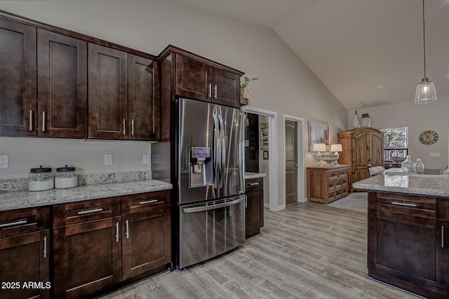 kitchen featuring stainless steel refrigerator with ice dispenser, light wood finished floors, hanging light fixtures, dark brown cabinetry, and light stone countertops