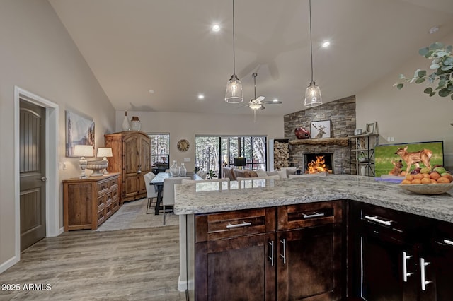 kitchen with light wood finished floors, hanging light fixtures, open floor plan, a stone fireplace, and high vaulted ceiling