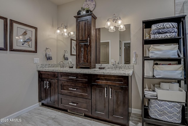 bathroom with marble finish floor, double vanity, a sink, and baseboards