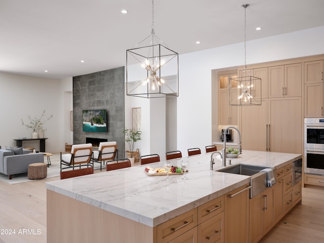 kitchen featuring an island with sink, sink, light brown cabinetry, a fireplace, and light hardwood / wood-style floors