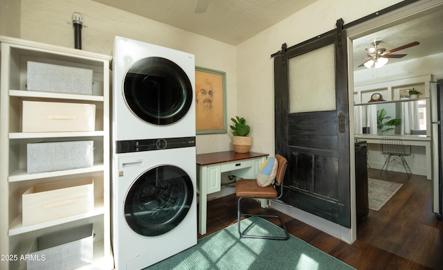 laundry area featuring dark hardwood / wood-style floors, a barn door, ceiling fan, and stacked washing maching and dryer