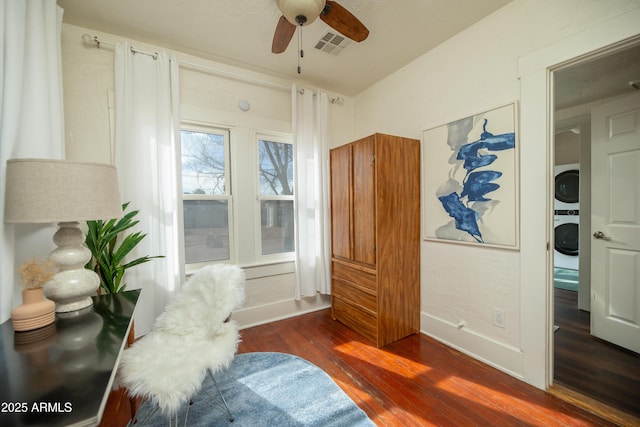 sitting room with stacked washing maching and dryer, dark hardwood / wood-style floors, and ceiling fan