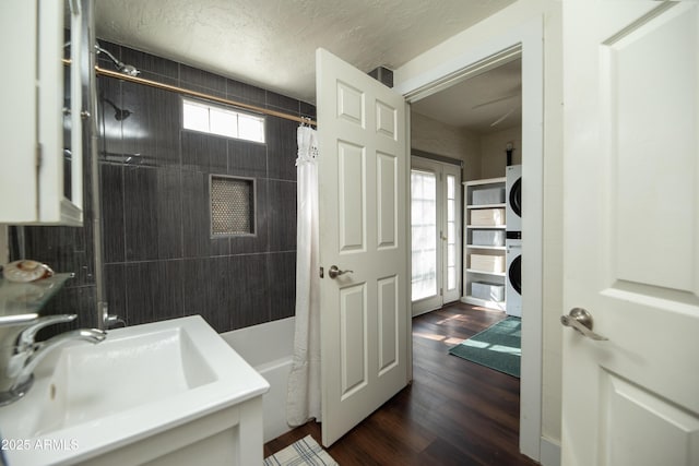 bathroom featuring stacked washer and clothes dryer, sink, shower / bath combination with curtain, a textured ceiling, and hardwood / wood-style flooring