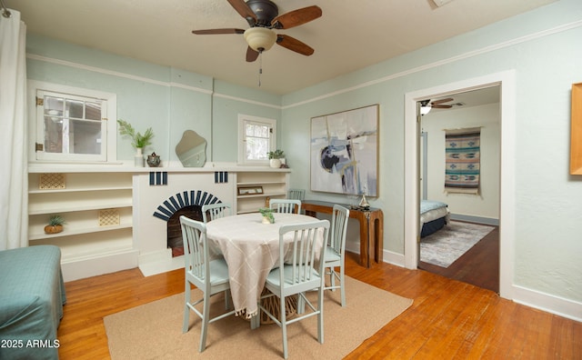 dining area featuring hardwood / wood-style flooring, ceiling fan, and a fireplace