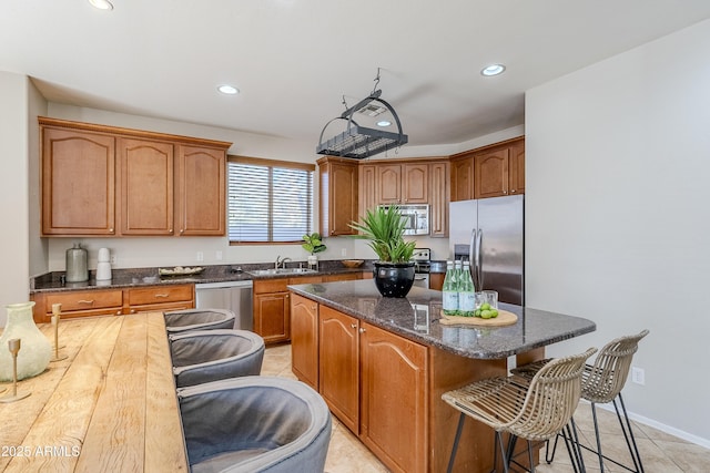 kitchen with light tile patterned floors, a kitchen island, appliances with stainless steel finishes, dark stone countertops, and sink