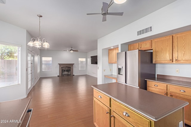 kitchen with ceiling fan with notable chandelier, a center island, dark hardwood / wood-style flooring, hanging light fixtures, and stainless steel fridge