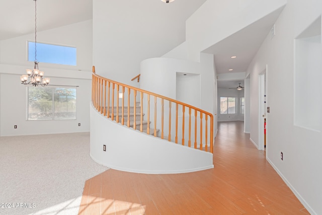 staircase with high vaulted ceiling, plenty of natural light, ceiling fan with notable chandelier, and hardwood / wood-style floors