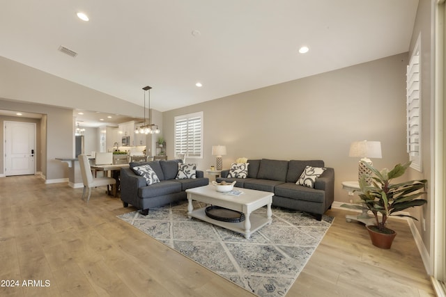 living room featuring a notable chandelier, light wood-type flooring, and lofted ceiling