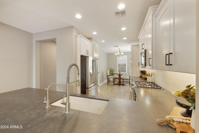 kitchen featuring sink, hanging light fixtures, stainless steel appliances, a notable chandelier, and white cabinets