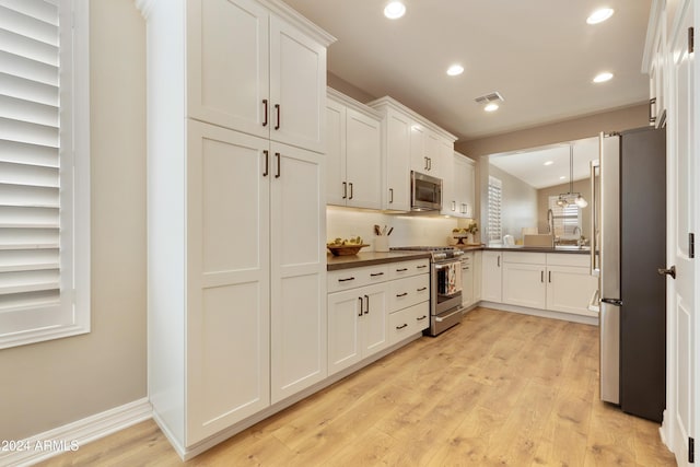 kitchen with white cabinets, stainless steel appliances, decorative light fixtures, and light hardwood / wood-style floors