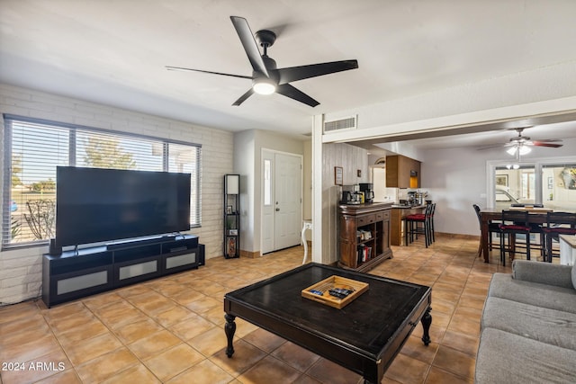 living room with light tile patterned flooring, ceiling fan, and brick wall