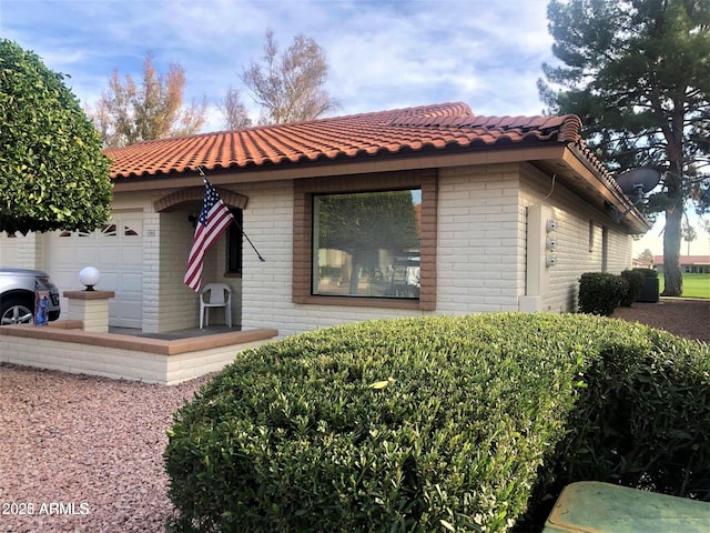 view of home's exterior with a tiled roof, brick siding, and an attached garage