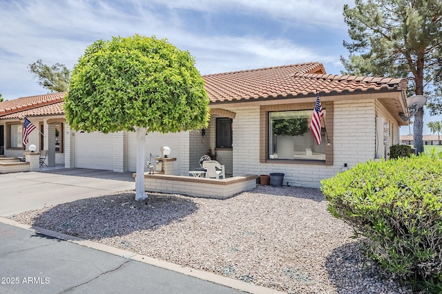 mediterranean / spanish home featuring brick siding, an attached garage, driveway, and a tile roof