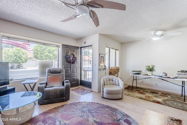 living area with a ceiling fan, baseboards, hardwood / wood-style flooring, and a textured ceiling