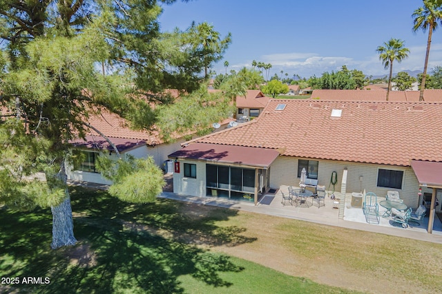 rear view of property featuring a lawn, a patio area, a tile roof, and brick siding