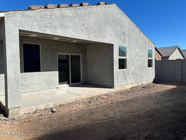 rear view of property with stucco siding, a patio, and fence