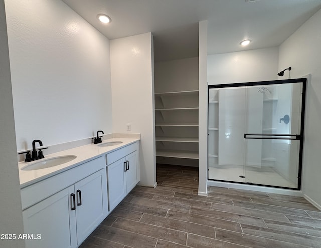 bathroom featuring a sink, a shower stall, wood tiled floor, and double vanity