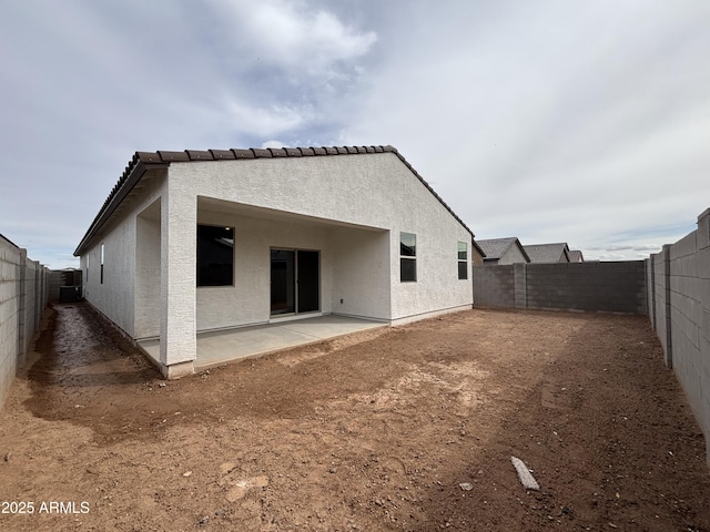 rear view of house featuring a tiled roof, stucco siding, a fenced backyard, and a patio area