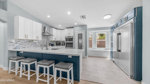 kitchen featuring stainless steel appliances, a peninsula, decorative backsplash, wall chimney range hood, and a breakfast bar area