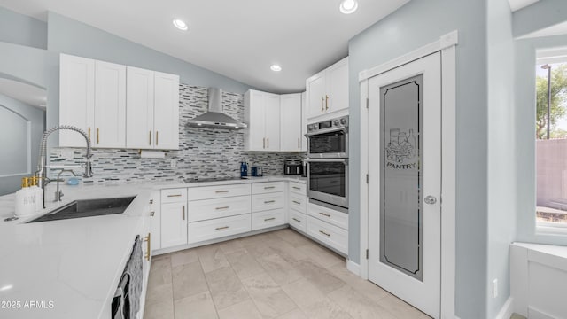 kitchen with wall chimney range hood, a sink, decorative backsplash, vaulted ceiling, and white cabinets