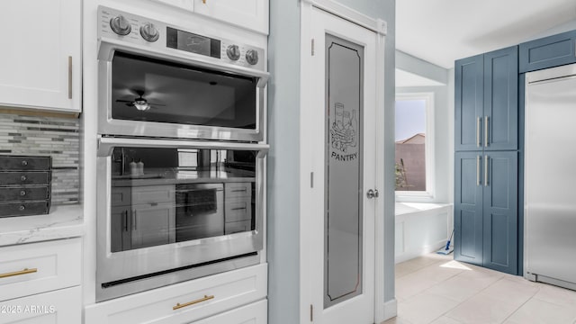 kitchen with stainless steel appliances, tasteful backsplash, light stone counters, light tile patterned floors, and white cabinetry