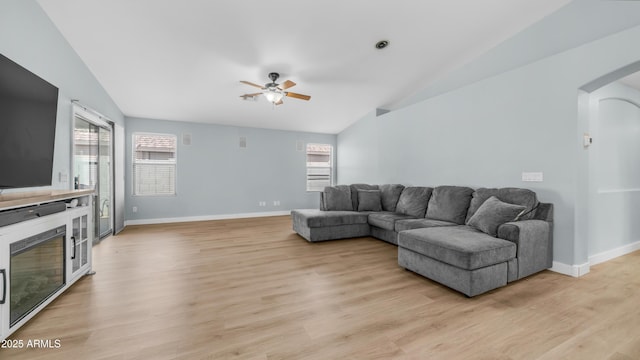 living area with lofted ceiling, arched walkways, a ceiling fan, baseboards, and light wood-type flooring