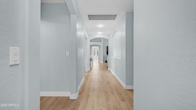 corridor featuring arched walkways, light wood-type flooring, and baseboards