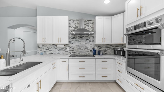 kitchen with a sink, stainless steel double oven, wall chimney exhaust hood, vaulted ceiling, and black electric cooktop
