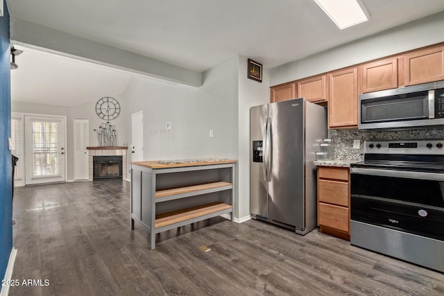 kitchen with dark wood-type flooring, stainless steel appliances, a tiled fireplace, and tasteful backsplash