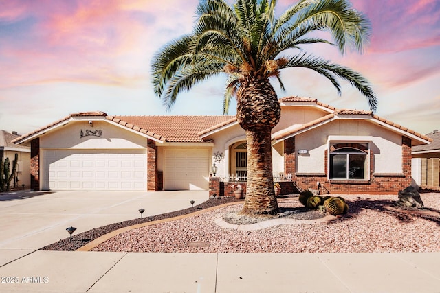 mediterranean / spanish-style home featuring brick siding, driveway, an attached garage, and stucco siding