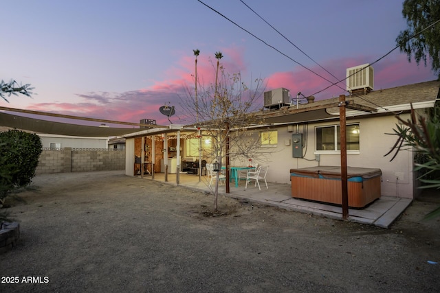 back house at dusk with a patio area, a hot tub, and central AC unit