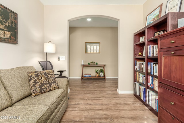 living room featuring arched walkways, baseboards, and wood finished floors