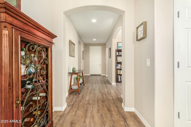 hall with arched walkways, wood finished floors, and baseboards