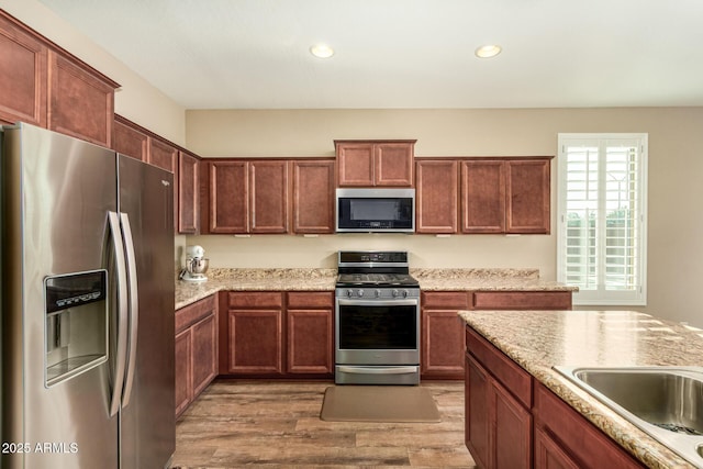 kitchen with recessed lighting, a sink, appliances with stainless steel finishes, light wood-type flooring, and light stone countertops