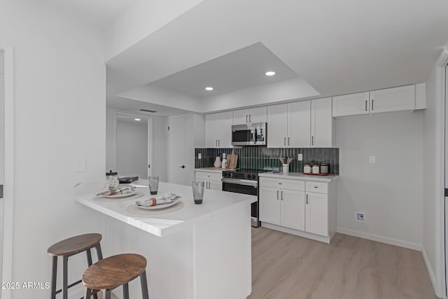 kitchen featuring a kitchen breakfast bar, electric range, white cabinets, and tasteful backsplash