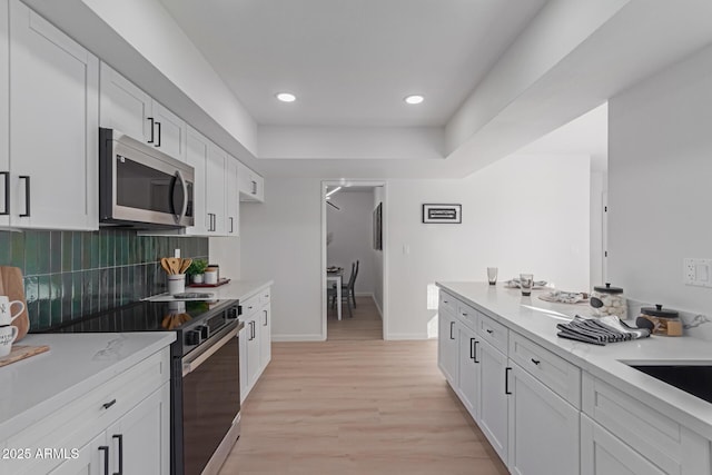 kitchen featuring decorative backsplash, electric range oven, white cabinetry, and light hardwood / wood-style floors