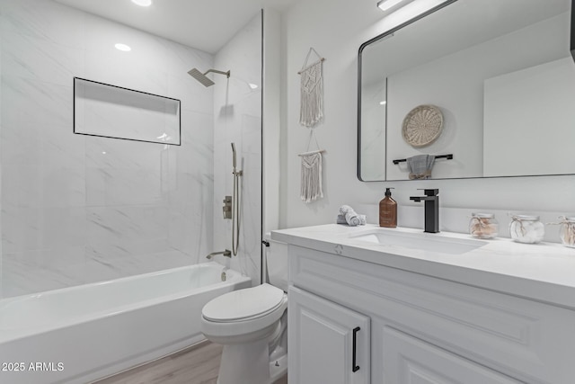 full bathroom featuring wood-type flooring, tiled shower / bath combo, vanity, and toilet