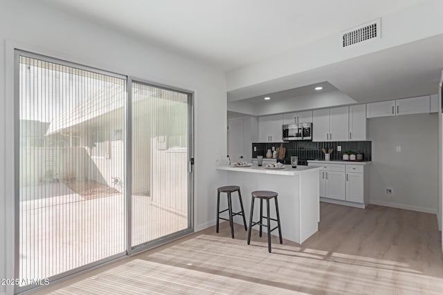 kitchen with white cabinetry, a kitchen bar, kitchen peninsula, backsplash, and light hardwood / wood-style flooring