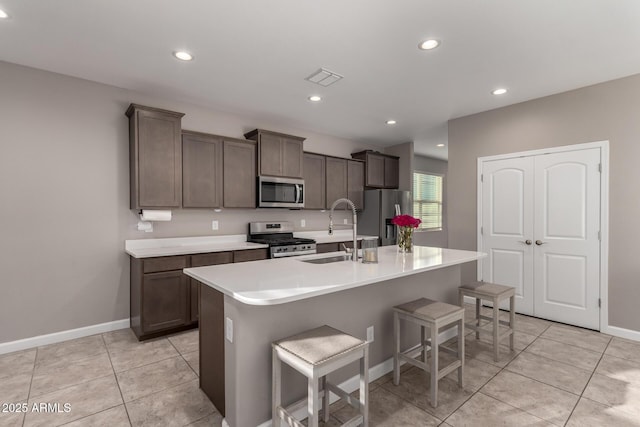 kitchen featuring a kitchen island with sink, a sink, light countertops, appliances with stainless steel finishes, and a kitchen bar