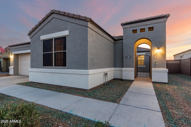 view of front facade with stucco siding, concrete driveway, a gate, fence, and a garage